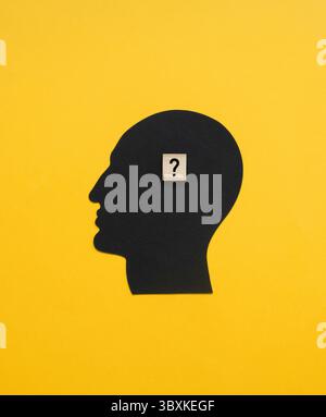 Symbol eines Pensigen Mannes, der eine Frage hat und auf eine Antwort wartet. Komposition mit schwarzem Menschenkopf und Holzblock mit schwarzem Fragezeichen. Stockfoto