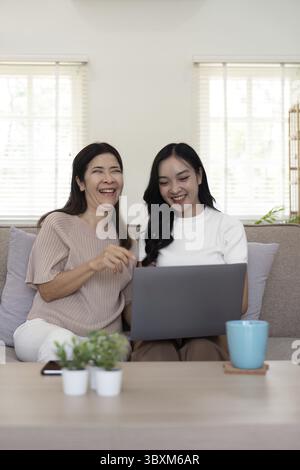 Seniorenmutter und Erwachsene Tochter entspannen sich und schauen sich zu Hause gemeinsam den Laptop an Stockfoto