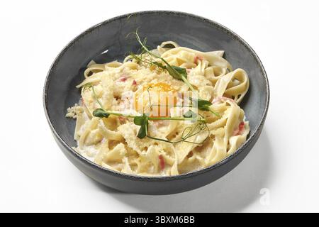 Klassische italienische Creme aus Fettuccine Carbonara mit Pancetta und Eigelb, garniert mit geriebenem Parmesan und Mikrogrün, präsentiert in cera Stockfoto