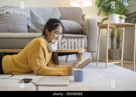Die junge hübsche Frau, die auf dem Boden liegt und ein Buch liest, genießt Ruhe. Entspannen zu Hause Stockfoto
