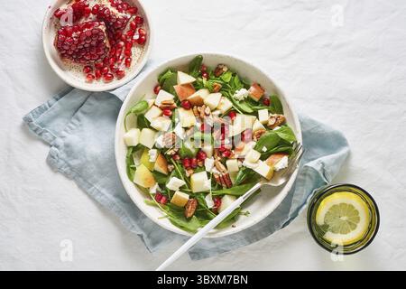 Obstsalat mit Nüssen, ausgewogenes Essen, sauberes Essen. Spinat mit Äpfeln, Pekannüssen und Feta, garniert mit Granatapfelkernen in einer Schüssel auf dem Tisch mit Weißwein Stockfoto