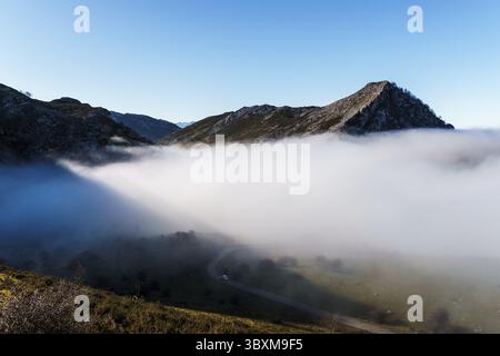 Misty Mountain Valley Road Scene, eine gewundene Straße schlängelt sich durch den Talboden mit Bergen, die auf beiden Seiten aufsteigen, teilweise von einem dicken L verdeckt Stockfoto