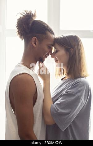 Porträt eines multirassischen Paares, Freund und Freundin von Angesicht zu Angesicht, stehen in der Nähe des Fensters Stockfoto
