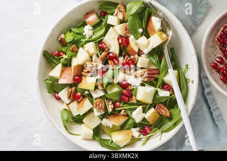 Obstsalat mit Nüssen, ausgewogenes Essen, sauberes Essen. Spinat mit Äpfeln, Pekannüssen und Feta, garniert mit Granatapfelkernen in einer Schüssel auf dem Tisch mit Weißwein Stockfoto