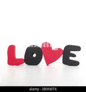 WORTLIEBE aus roten und schwarzen volumetrischen Buchstaben und Herz auf weißem Hintergrund. Valentinstag, Liebestag und Hochzeitskonzept. Vertikales Foto. Stockfoto