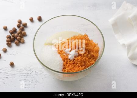 Essen, Glasschale mit Grieß, Eiern, geriebenen Karotten, Zucker, Salz und Backpulver. Kochen von Mannik, Kuchen oder Kuchen auf hellblauem Hintergrund. Schritt für Schritt Stockfoto