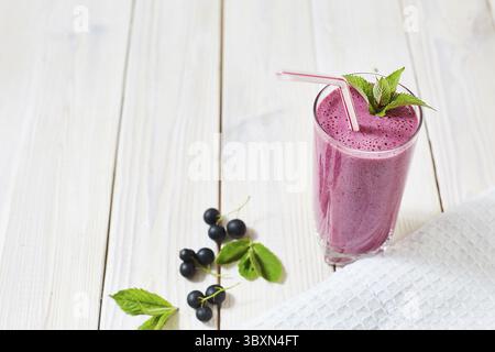 Vitamincocktail aus schwarzen Johannisbeeren, Eis, Milch in einem Glasbecher. Kunststoffrohr und Minze Stockfoto