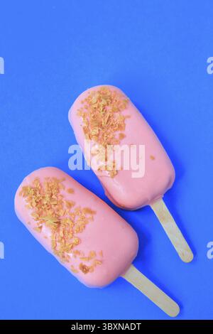 Kuchen - Eis in rosa Glasur und Krümel auf blauem Hintergrund. Leerzeichen für Text. Eiscreme süßes eskimo mit Schokoladenglasur. Mit Schokolade überzogenes Eis Stockfoto