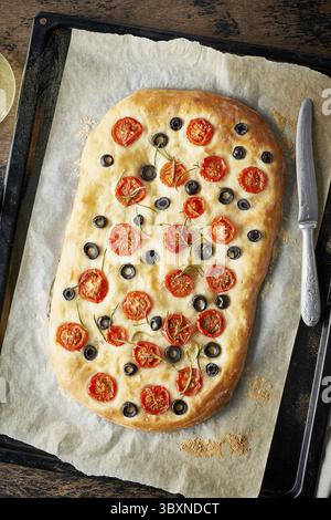 Focaccia, Pizza, italienisches Fladenbrot mit Tomaten, Oliven und Rosmarin auf Tablett auf dunklem Holztisch, Blick von oben, vertikal Stockfoto