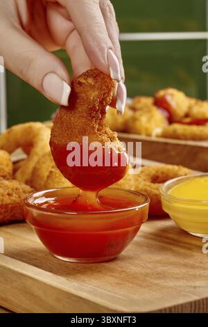 Nahaufnahme von panierten Hähnchennuggets in scharfer Ketchup-Sauce mit Zwiebelringen und Senf im Hintergrund Stockfoto