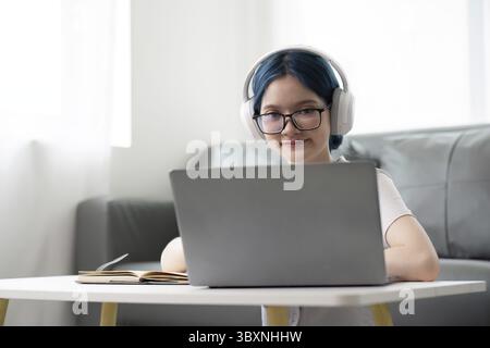 Glückliche junge Frau im Teenageralter mit Kopfhörern, Schreibzettel. Schüler Online-Lernkurs lernen Online-Videoanruf Zoomlehrer mit Laptop und Buch Stockfoto