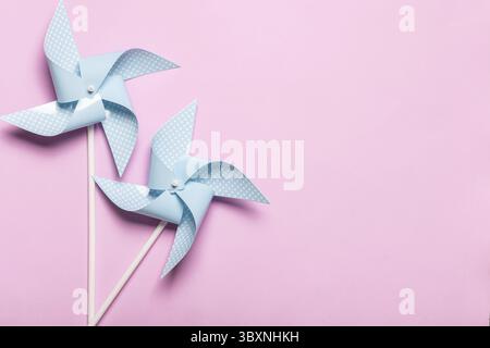 Blaues Papier dreht sich auf hellrosa Hintergrund. Kinderspielzeug bunte Räderchen auf Partyhintergrund. Draufsicht, flach Stockfoto