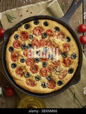 Focaccia, Pizza in Pfanne, italienisches Fladenbrot mit Tomaten, Oliven und Rosmarin. Vertikal, ein Holztisch Stockfoto