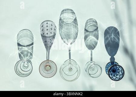 Leere Gläser verschiedener Formen für weiß-, Rot- und Rosenwein stehen in Reihe auf blauem Hintergrund im Sonnenlicht mit Schatten. Draufsicht, flach. Stockfoto