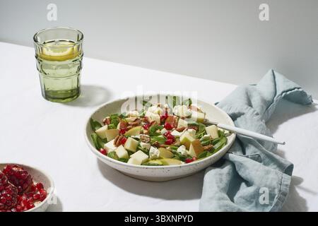 Obstsalat mit Nüssen, ausgewogenes Essen, sauberes Essen. Spinat mit Äpfeln, Pekannüssen und Feta, garniert mit Granatapfelkernen in einer Schüssel auf dem Tisch mit Weißwein Stockfoto