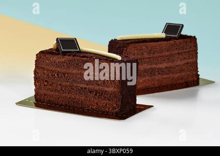 Zwei köstliche Schokoladenkuchenscheiben, die mit knusprigen Streuseln überzogen sind und auf goldenen Basen vor pastellblauem und gelbem Hintergrund präsentiert werden Stockfoto