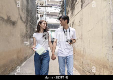 Ein Paar schlendert Hand in Hand durch eine lebhafte urbane Gasse und hält ihre Reisemomente mit Freude und Liebe fest Stockfoto