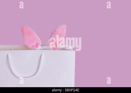 Nahaufnahme von lustigen rosa Ohren des Osterhasen, die aus einer weißen Geschenktüte auf rosa Hintergrund stehen. Kopierbereich. Happy Easter-Konzept Stockfoto