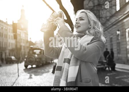 Junge schöne, fröhliche blonde Frau, die an einem sonnigen Tag auf dem Rynok-Platz in Lemberg, Ukraine, Fotos mit ihrer Vintage-Filmkamera macht Stockfoto