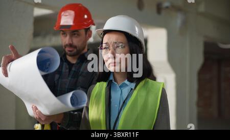 Bauinspektion multiethnische Baumeister Architekten sprechen Bauplan vor Ort Kaukasischer Mann Ingenieur halten Bauplan diskutieren asiatische Frau Stockfoto