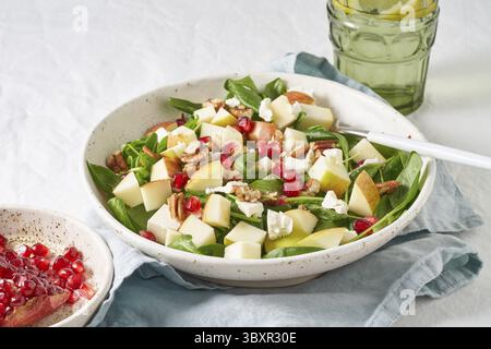 Obstsalat mit Nüssen, ausgewogenes Essen, sauberes Essen. Spinat mit Äpfeln, Pekannüssen und Feta, garniert mit Granatapfelkernen in einer Schüssel auf dem Tisch mit Weißwein Stockfoto