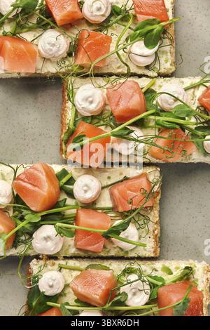 Aus nächster Nähe sehen Sie vier appetitliche Sandwiches mit Lachs, Frischkäse, Erbsensprossen und Meringue, die auf einem Teller angeordnet sind Stockfoto