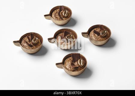 Handgemachte Schokoladenbonbons mit reichhaltiger Kaffeesahne, künstlerisch gestaltet, um wie kleine Kaffeetassen vor weißem Hintergrund aussehen zu lassen Stockfoto