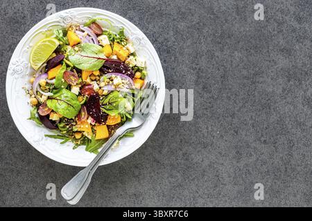 Essen, frischer Gemüsesalat mit Roter Bete, Rucola, roten Zwiebeln, Sauerampfer, Kichererbsen, Kürbis und Trauben auf einem weißen Teller auf schwarzem Hintergrund Stockfoto