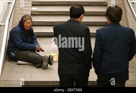 28. März 2006, PEKING, CHINA: Am 28. März 2006 bettelt eine alte Frau Geschäftsleute um Geld auf den Straßen von Peking, China. Ohne ein nationales Sozialsystem oder ein soziales Sicherungsnetz, um diejenigen zu fangen, die dringend medizinische Hilfe benötigen, sind viele verkrüppelte und behinderte Chinesen gezwungen, sich selbst zu wehren und landen normalerweise auf der Straße. Eine große Sorge unter den Chinesen, die unter den harten Wirtschaftsreformen leiden, die vor einigen Jahren durchgeführt wurden und viele staatliche Unternehmen geschlossen haben, ist die faktische Abschaffung des staatlichen Wohlfahrtssystems, das sie einst von Geburt bis zum Tod betreute. (Kredit Ima Stockfoto