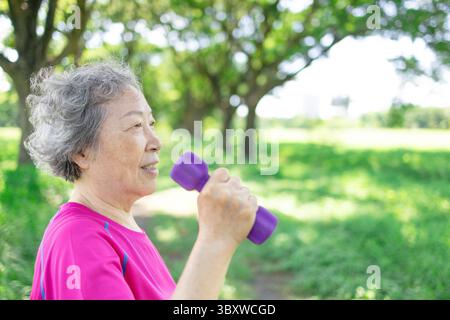 Glückliche asiatische Seniorin, die Hantel hebt Stockfoto