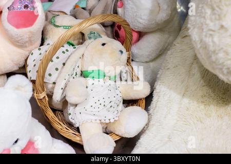 Ein farbenfroher Korb, gefüllt mit einer Vielzahl von Stofftieren, hervorstehend mit einem entzückenden Häschen in einem schönen weißen Kleid Stockfoto