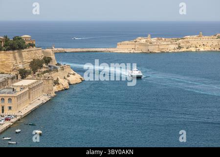 Valletta, Malta – 21. Juni 2021: Ein Katamaran von Virtu Ferries verlässt den Grand Harbour, vorbei an historischen Bastionen und Küstenarchitektur. Stockfoto