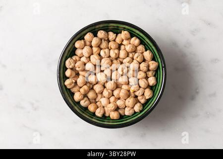Schüssel Kichererbsen auf Marmor. Gesunde vegane Proteinnahrung. Bio-Leguminosen-Inhaltsstoff. Trockene Garbanzo-Bohnen, Draufsicht. Vegetarische Küche. Stockfoto