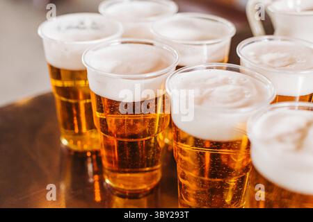 Mehrere Plastikbecher gefüllt mit Bier. Frischer Schaum auf goldenem Lager. Erfrischende kalte Getränke für Partys oder Veranstaltungen. Alkoholisches Getränk auf Metall. Stockfoto