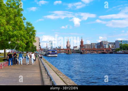 Berlin, Deutschland - 30. Mai 2025: Sonniger Tag an der Spree in Berlin, an dem Menschen entlang der Promenade mit der Oberbaumbrücke im Backgr. Spazieren Stockfoto