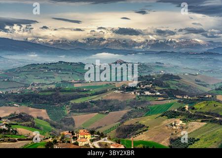 Herrliches Panorama der bewirtschafteten Hügel rund um Ripatransone mit den schneebedeckten Gipfeln der Sibillini-Berge im Hintergrund. Marken Stockfoto