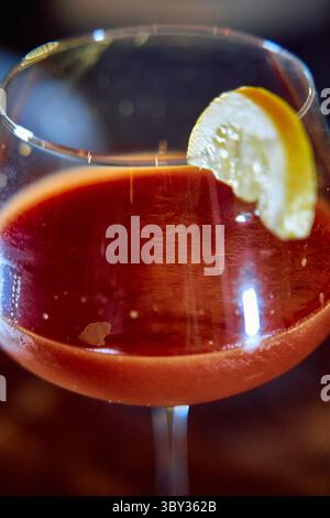Ein lebhafter, roter Cocktail, elegant im Glas präsentiert, garniert mit einer erfrischenden Zitrusscheibe, perfekt für Sommergenuss oder raffinierten Mixolog Stockfoto