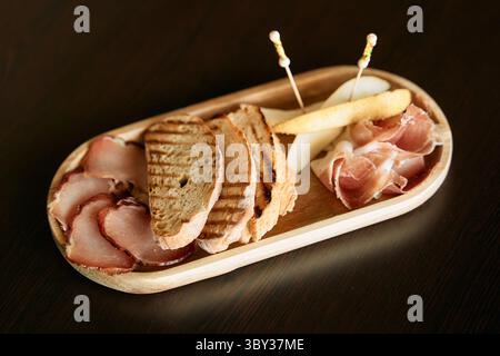 Auf dem schmackhaften Wurstteller finden Sie Räucherfleisch, geröstete Brotscheiben und Käse, der auf einer Holzplatte schön angeordnet ist Stockfoto