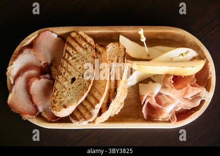 Eine rustikale Wurstplatte mit aufgeschnittenem Fleisch, Birnenscheiben und gegrilltem Brot, kreativ für eine appetitliche Präsentation und Gourmet-Snacks Stockfoto