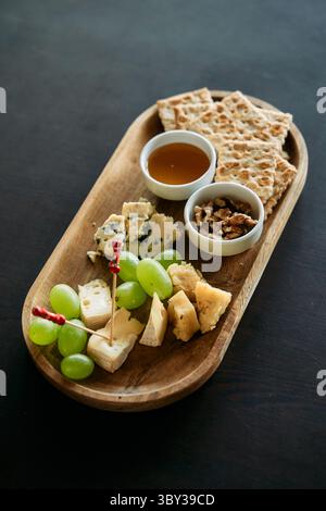 Eine Gourmet-Käseplatte mit verschiedenen Käsesorten, Trauben, Crackern, Honig und Nüssen auf einem Holztablett bietet eine elegante und köstliche Vorspeise. Stockfoto