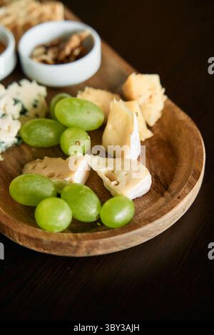 Ein elegantes Arrangement aus verschiedenen Käsesorten und grünen Trauben auf einem braunen Holztablett, perfekt für Gourmet-Snacks und Unterhaltung. Stockfoto