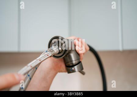 Nahaufnahme der Hände eines Klempners, die flexible Wasserversorgungsleitungen mit der Basis eines neuen Küchenarmators verbinden, demonstrieren den Prozess der Installation von Sanitäranlagen in einer modernen Küchenumgebung Stockfoto