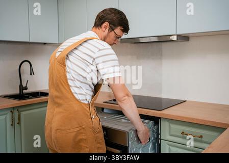 Professionelle Handwerker installieren sorgfältig einen neuen Ofen in einer renovierten Küche, um eine präzise Platzierung und sicheren Sitz innerhalb der Schränke zu gewährleisten Stockfoto
