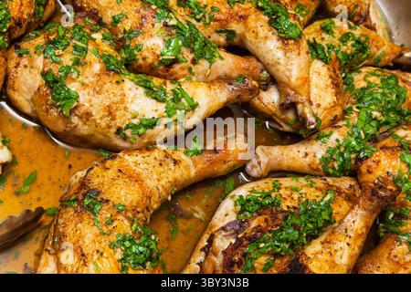 Gebackene Hähnchenschenkel in eigenem Fett, bestreut mit gehackter Petersilie und Knoblauch in einer Schüssel mit einer Zange Nahaufnahme. Stockfoto