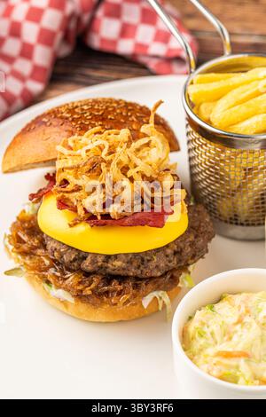 Köstlicher Gourmet-Burger mit Cheddar-Käse, gebratenen Zwiebeln, Krautsalat und Pommes frites Stockfoto