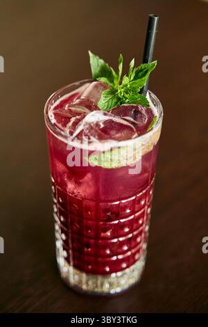 Ein lebendiger Cocktail aus Eisbeeren, garniert mit Minze und Limette, serviert in einem strukturierten Glas mit Strohhalm, das eine perfekte Mischung aus erfrischendem und süßem geschmack bietet Stockfoto