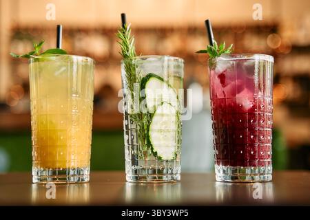Drei handwerklich hergestellte Cocktails mit Beilagen mit Zitrus-, Gurken- und Beerenaromen stehen in eleganten Gläsern an der Bar und bieten eine Erfrischung Stockfoto