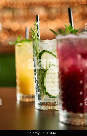 Eine lebhafte Show erfrischender Sommercocktails garniert mit Minze, Gurke und Beeren serviert in Kristallgläsern, vor einem festlichen Bokeh-bac Stockfoto