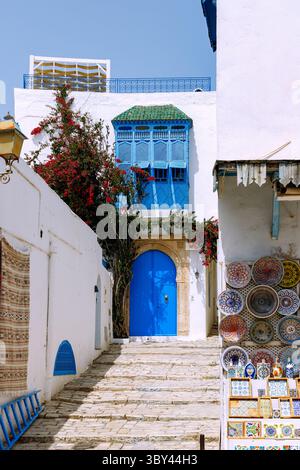 Treppe mit blauer Holztür und arabischem Balkon zwischen Souvenirläden in der (Medina) Altstadt von Sidi Bou Said, Tunesien Stockfoto