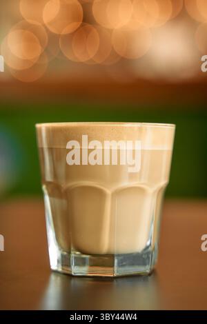 Eine Nahaufnahme eines cremigen Kaffees in einem Glas vor einem warmen Bokeh-Hintergrund. Ideal für gemütliche Café-Atmosphäre und entspannende Themen. Stockfoto